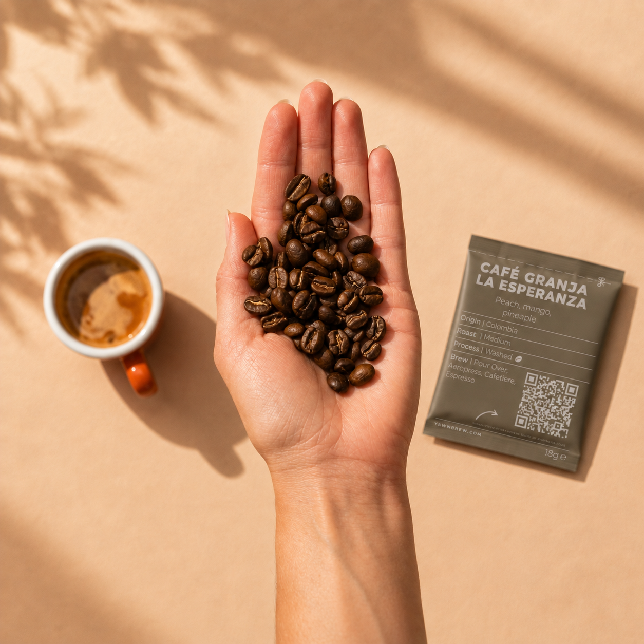 A hand holding coffee beans with advent sachet and mug on the table behind 